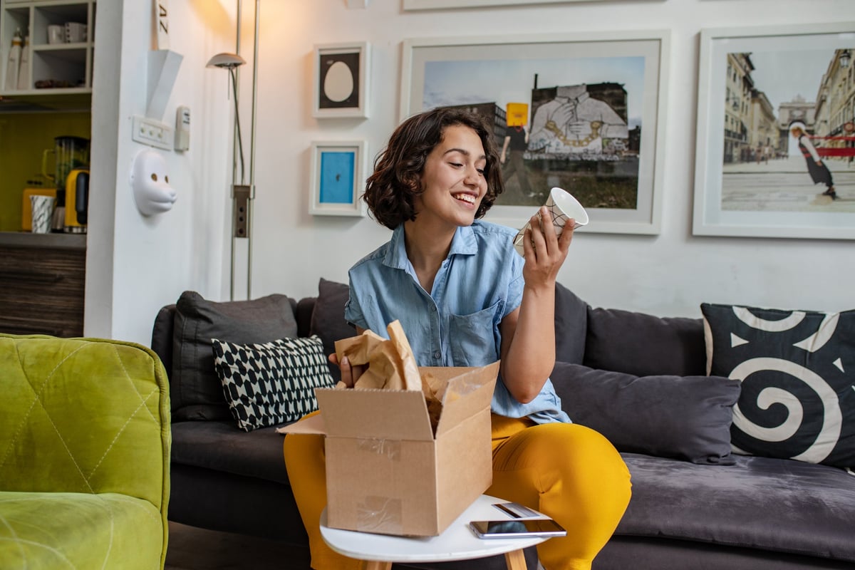 A young adult unpacks a delivered package on the couch.