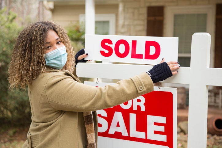 African American woman wearing a mask switches home For Sale sign to Sold.