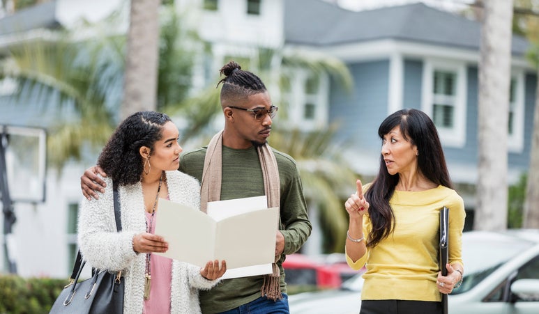 A real estate agent meeting in a parking lot with a young couple discussing mortgage documents.