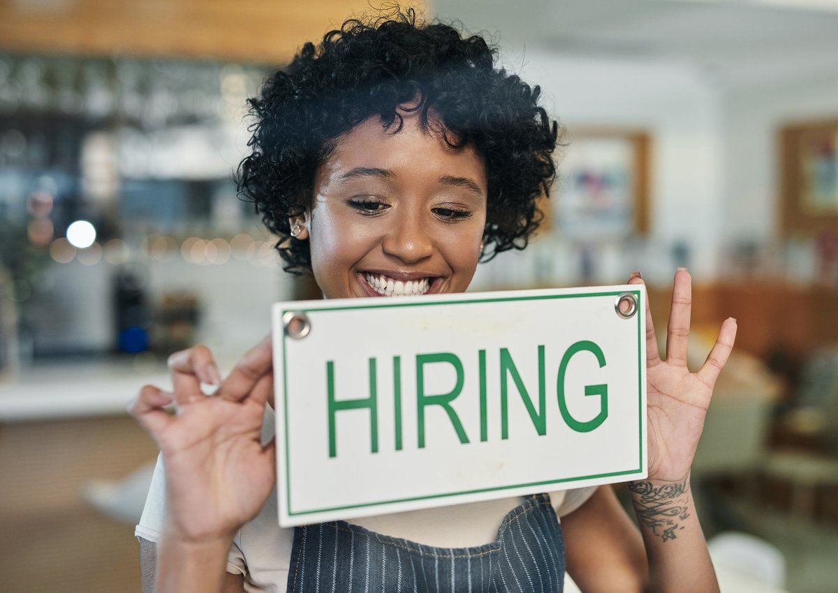 A business-owner puts up a Hiring sign on their shop's window.