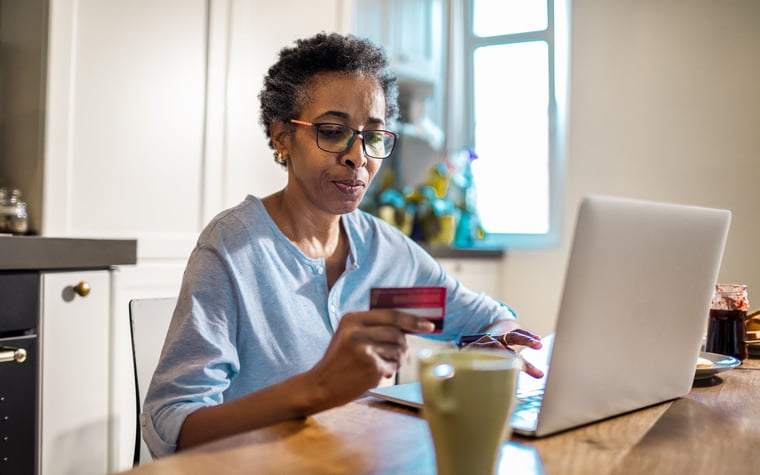 Une personne utilise une carte de crédit et un ordinateur portable pour acheter quelque chose en ligne dans sa cuisine.