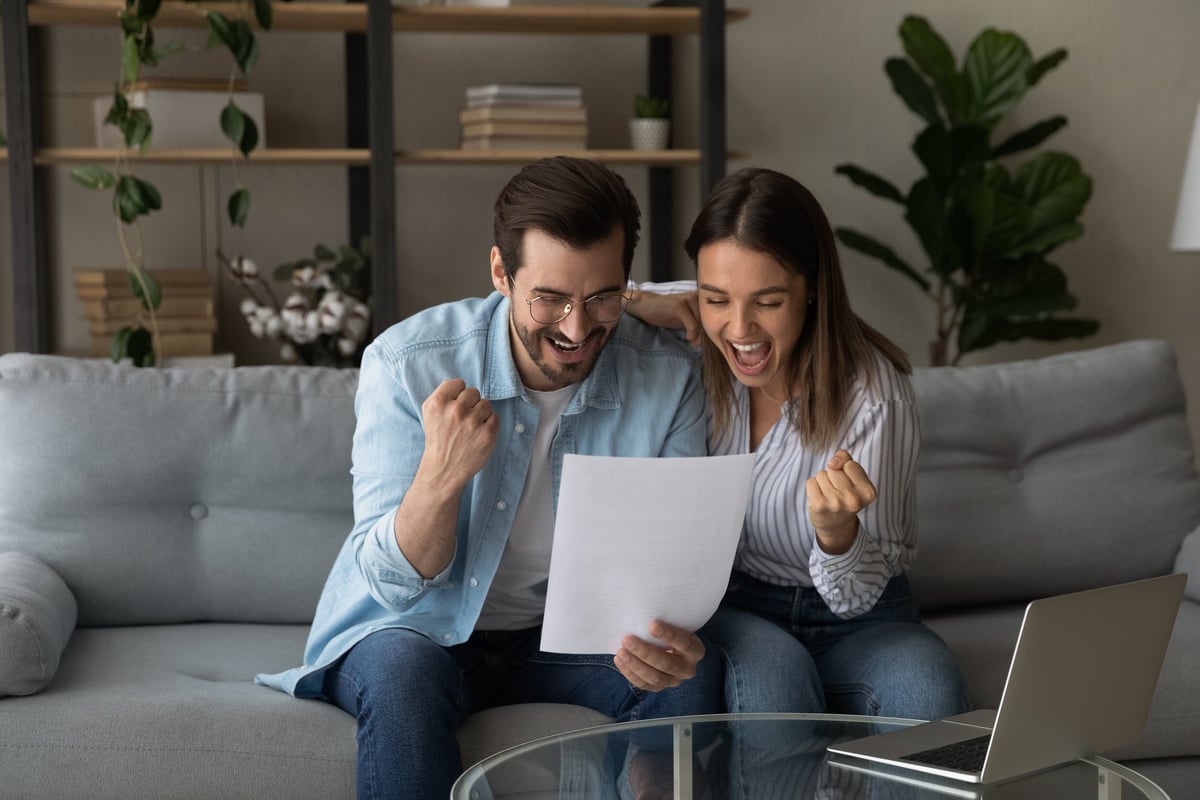 An overjoyed young couple pumps their fists while reading good news in a document together.