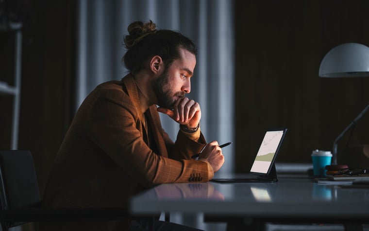 Une personne pensive lit un graphique sur un ordinateur portable dans un bureau tard dans la nuit.
