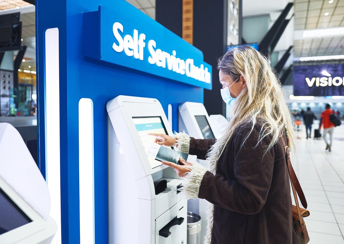 A young adult wearing a mask uses a kiosk to check in for a flight.