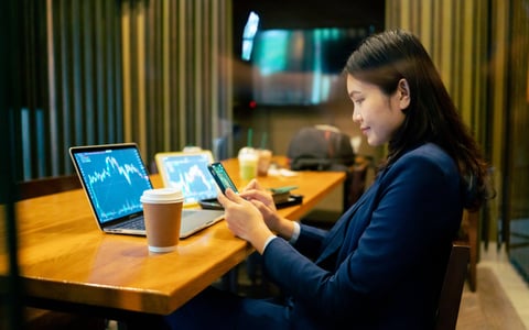 A smiling adult trades stocks using their mobile devices in a coffee shop.