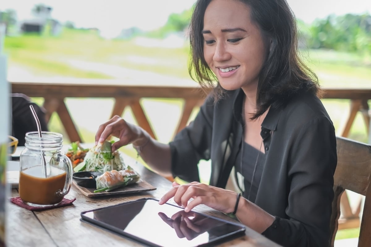 Someone happily uses a smart tablet while eating at a cafe outside.