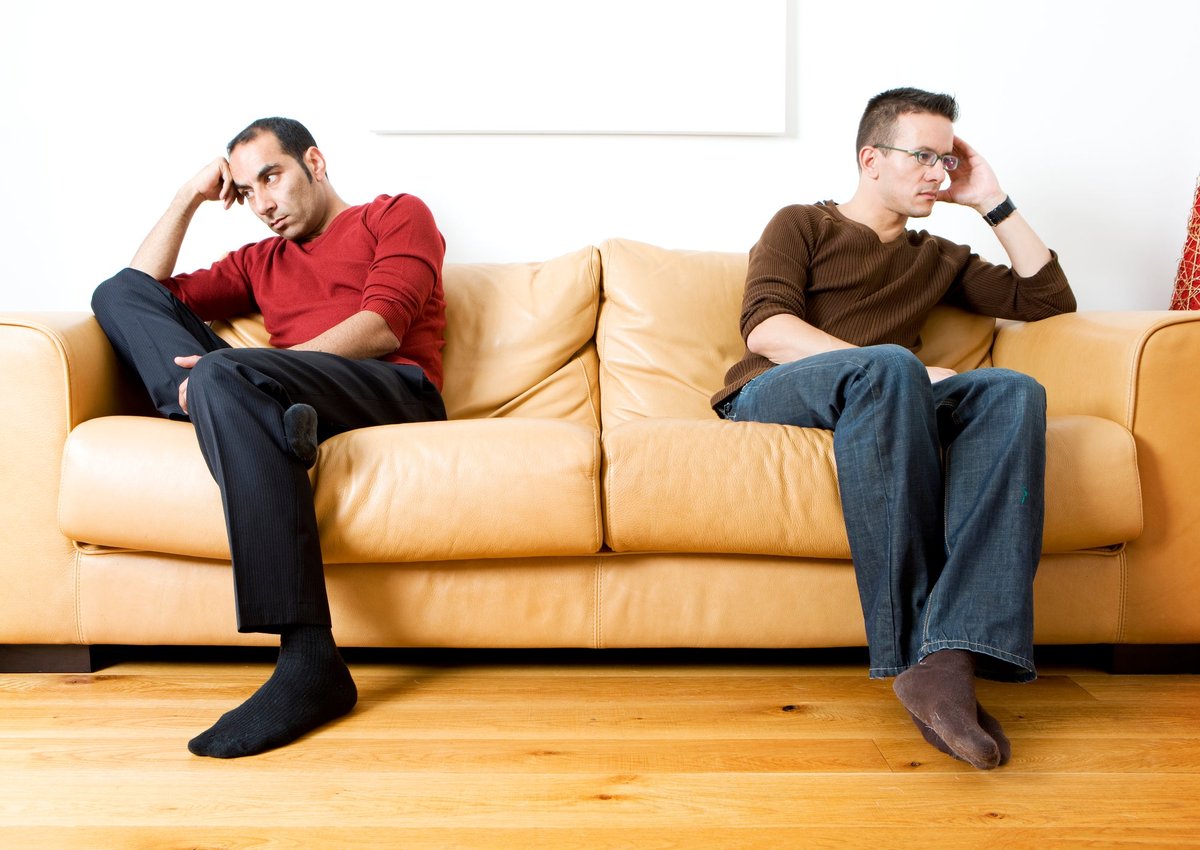 Two men sit on opposite ends of a couch, disgruntled.