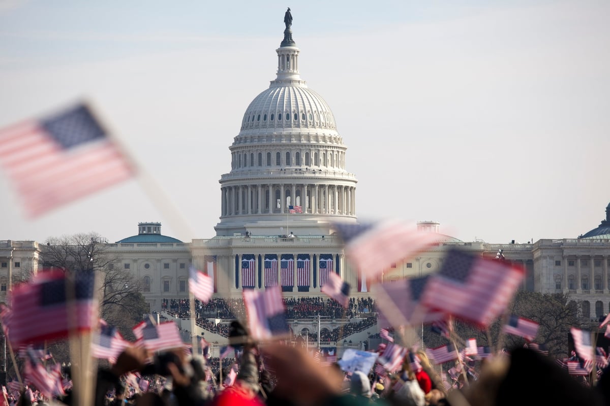 Unrecognizeable crowds waving American flags fill the Washington Mall in front of the Capitol building.