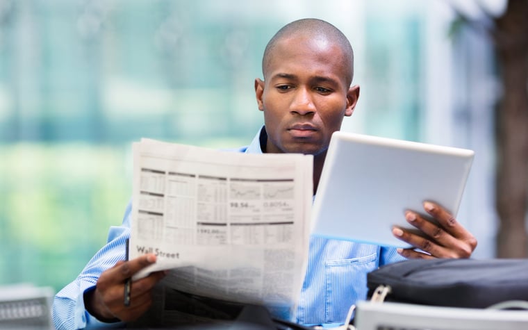 Man compares quotes from newspaper and tablet.