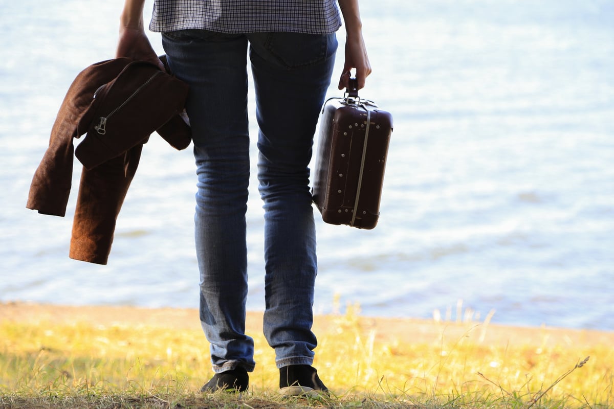 Man standing on riverbank with suitcase in tow.