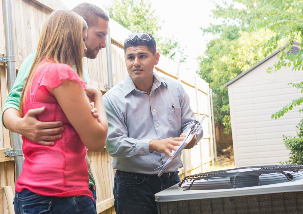 An air conditioner repairman uses a clipboard to explain the cost of repairs to the homeowners.