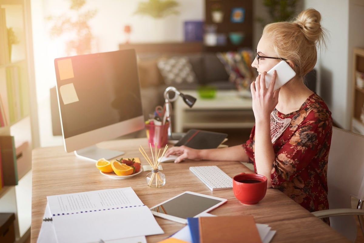 Young woman at home office desk using her cell phone.