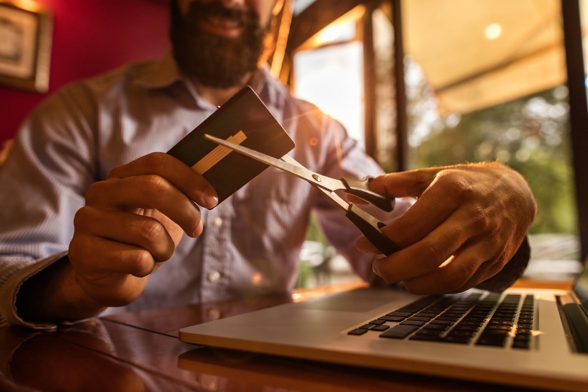 Man with massive beard cutting up credit card with pair of scissors.