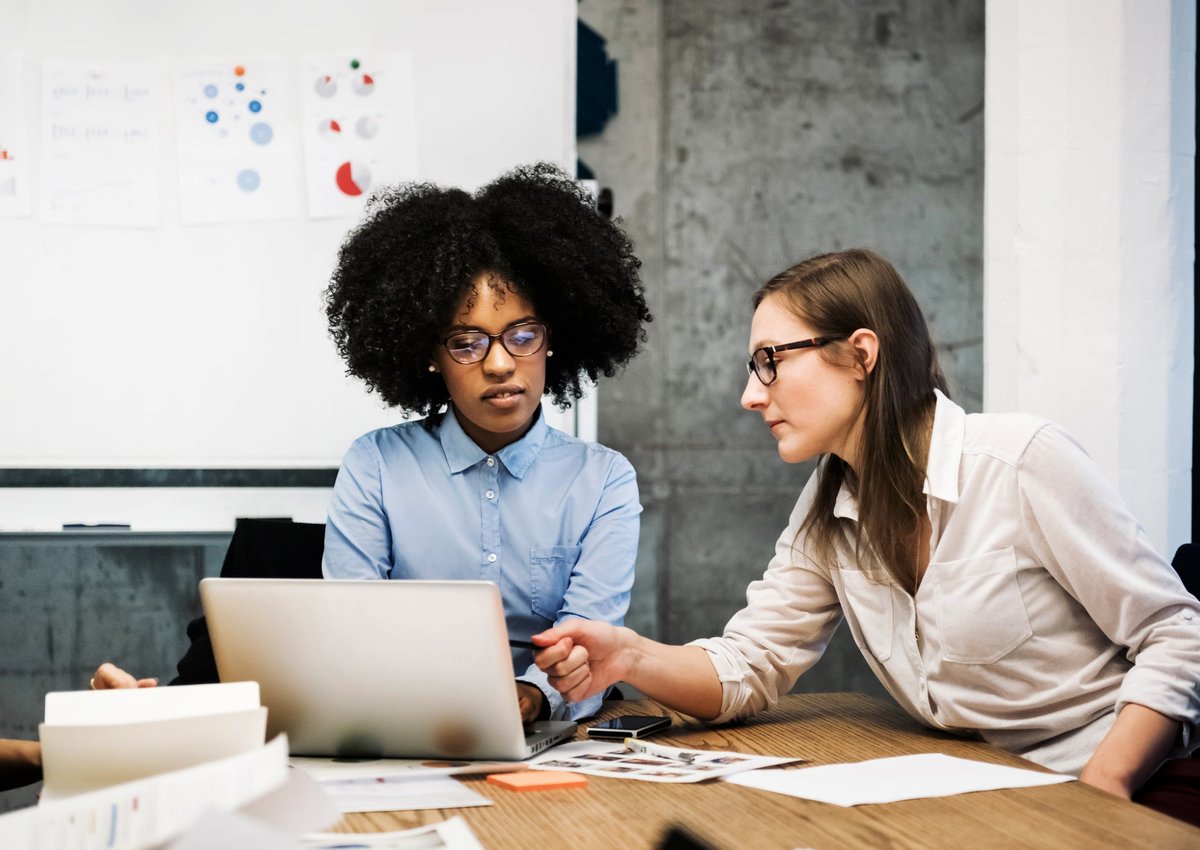 Two business people discussing pie charts and financial papers, one pointing at a computer screen.