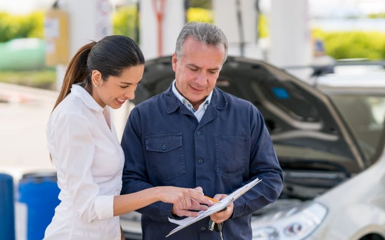 Young woman at a garage talking to a mechanic about her car. They both point at paperwork.