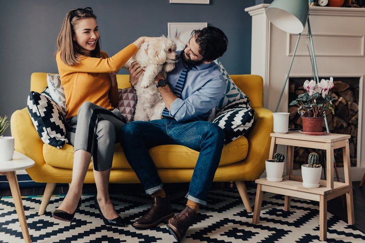 Couple qui rit sur un canapé avec un chien.