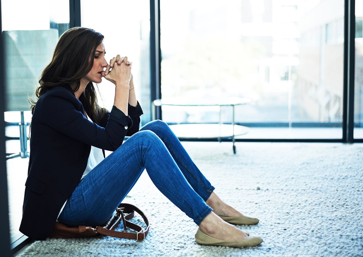 A depressed person holds hands stuck to his lips while sitting on the floor in the office.