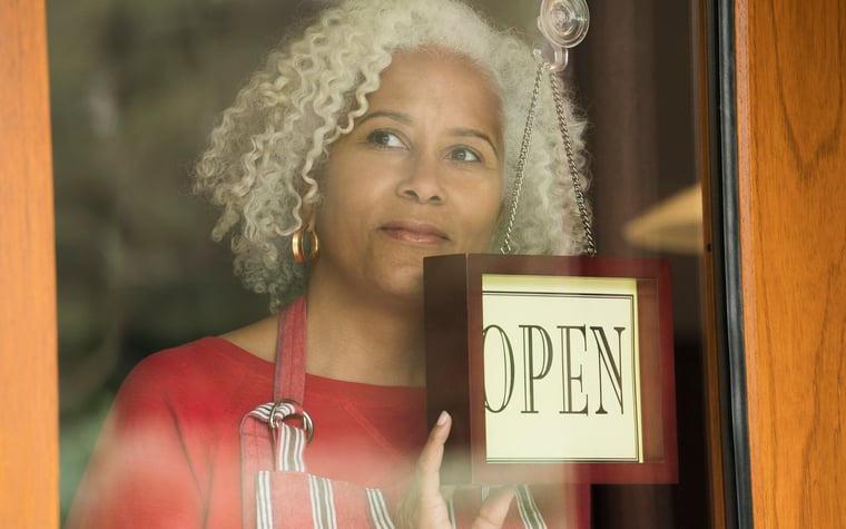 A person holds the "Open" sign on the front door of a small business.