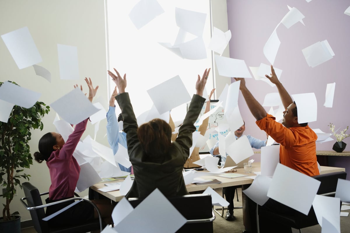 A group of office workers throw papers in the air excitedly.