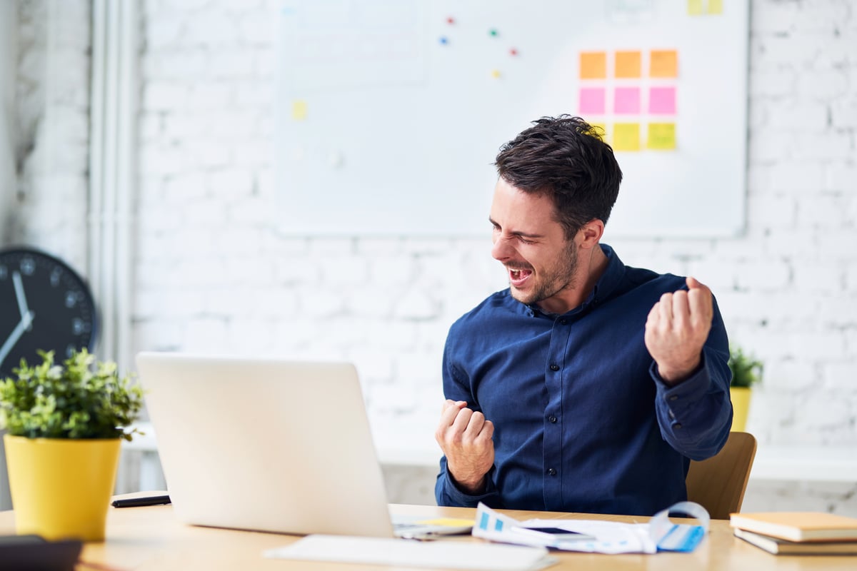 Man sitting at desk celebrating with fist up