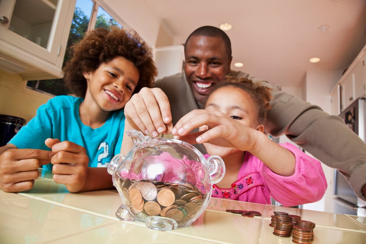 A parent watches their children put coins into a piggy bank at home.