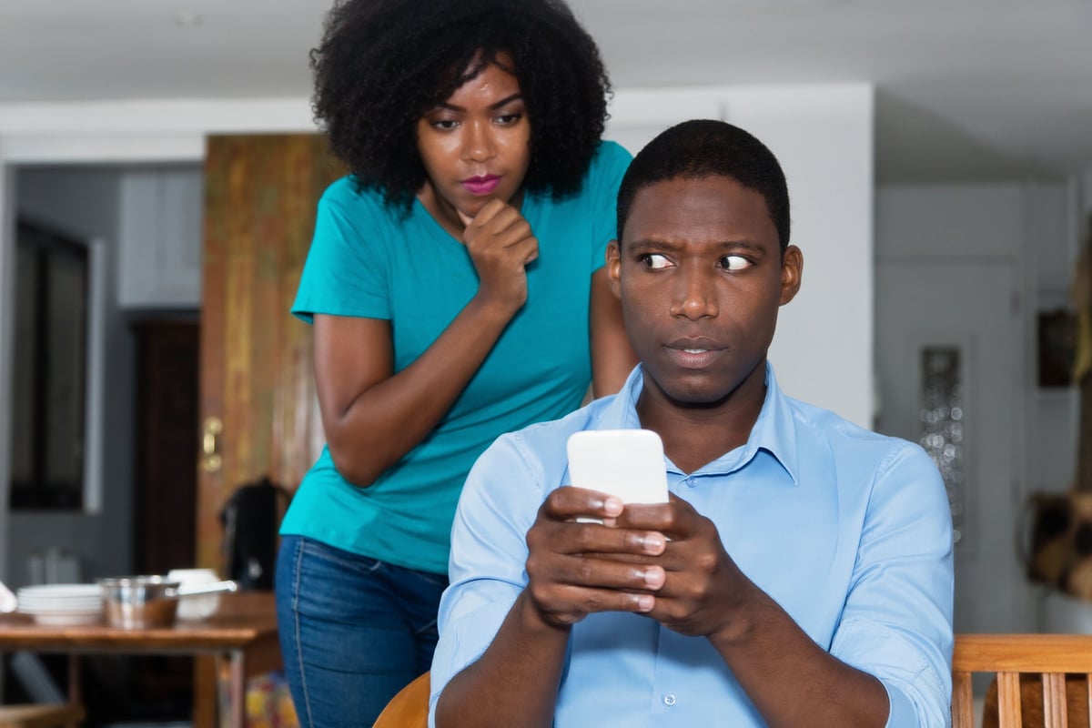 Woman looking over scared man's shoulder at his phone.