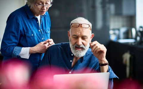 An older couple discusses something on a laptop screen.