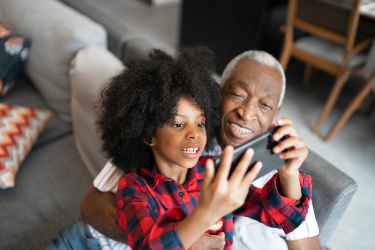 A grandparent watches as a grandchild plays a game on a phone.