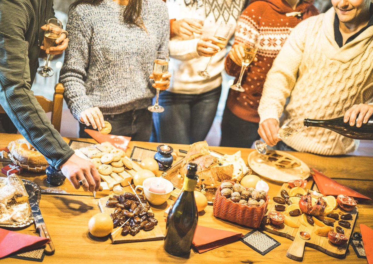 A group of friends in holiday sweaters gathered around platters of food and Champagne.