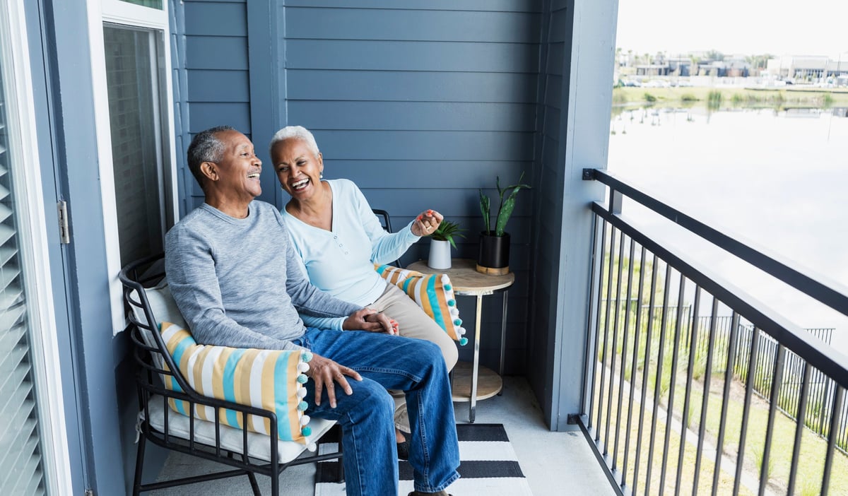 Happy mature couple sitting on balcony overlooking a pond.
