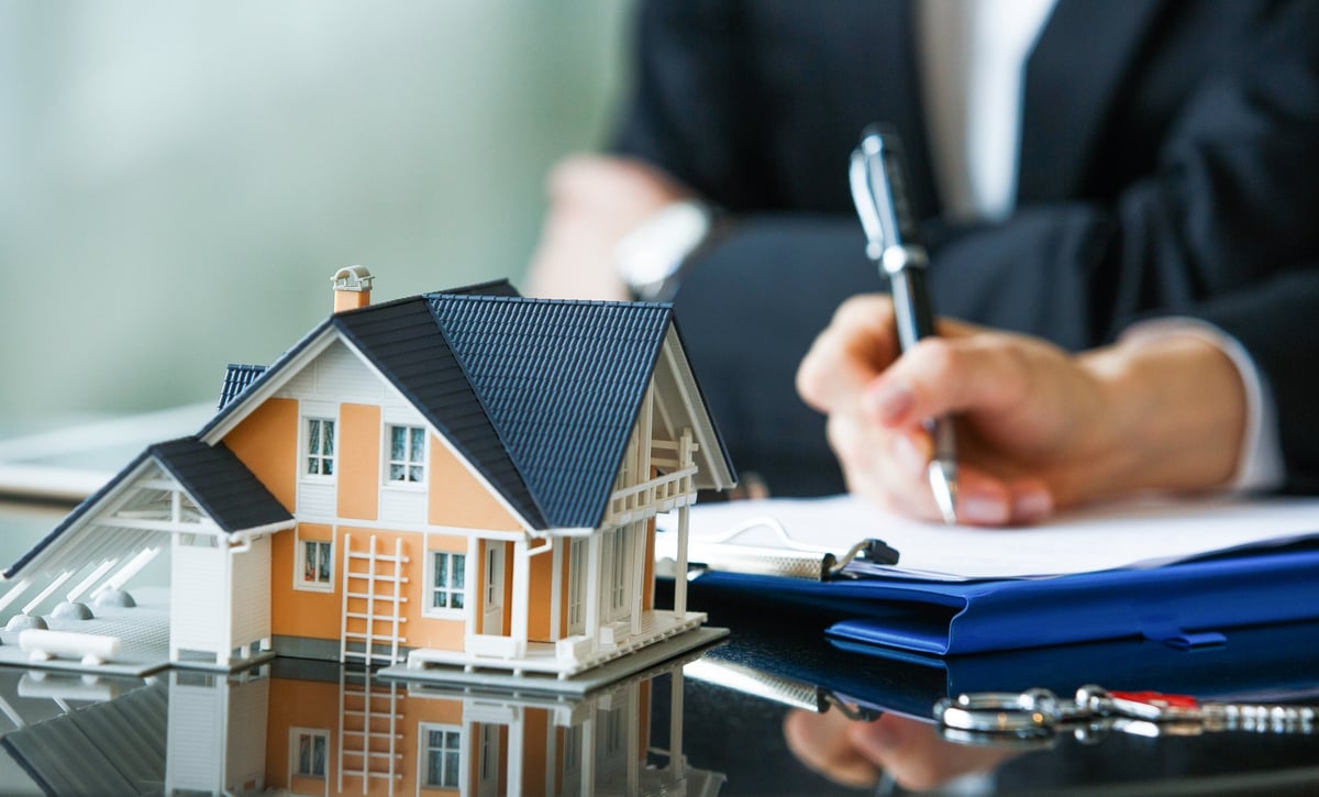 A person signing a piece of paper on a desk that has a model home on it.