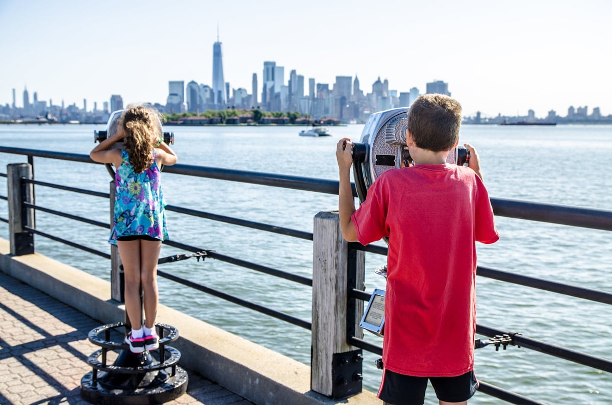 Children looking at Manhattan Island through paying binoculars from Liberty State Park in Jersey City during summer day.