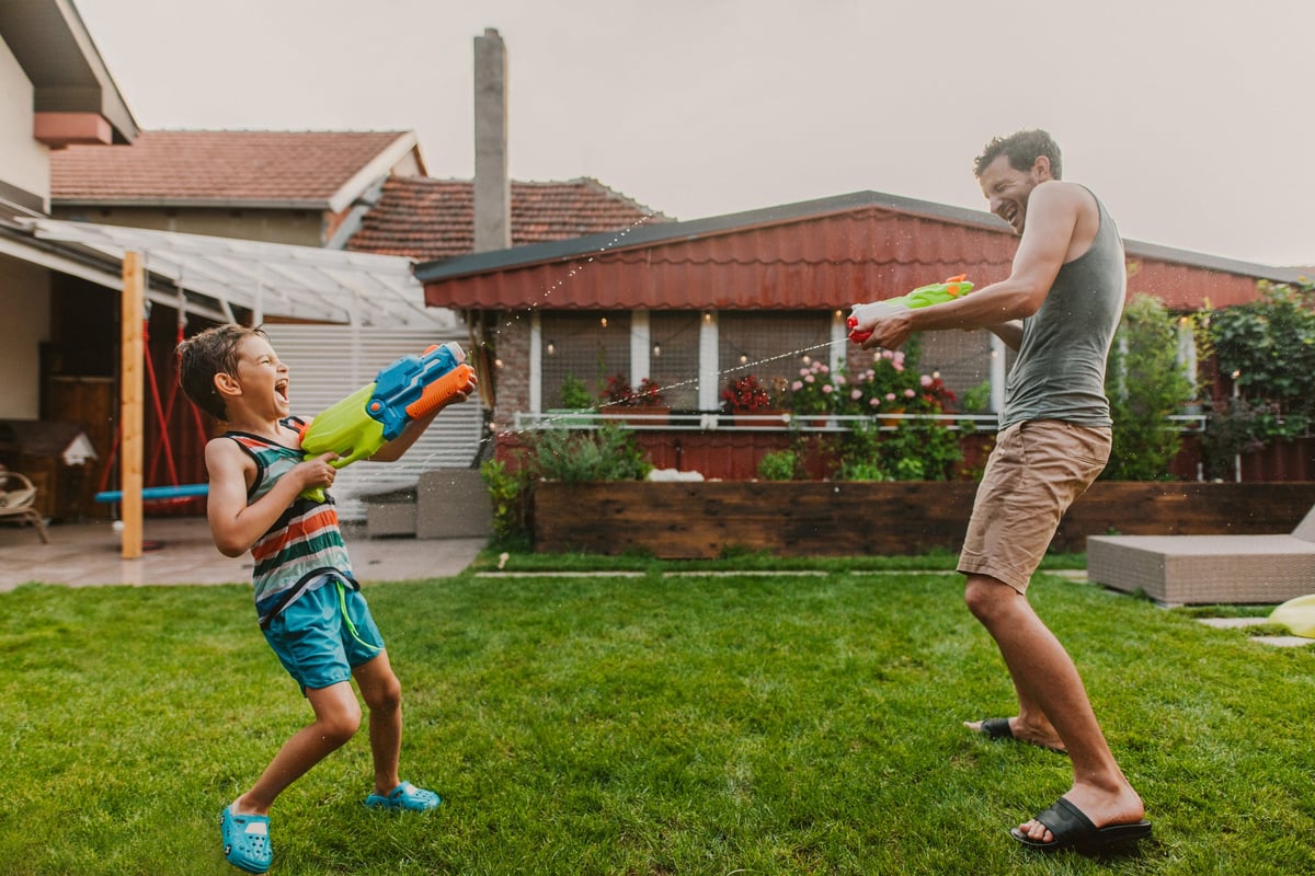 Man and child play with squirt guns in home's yard.