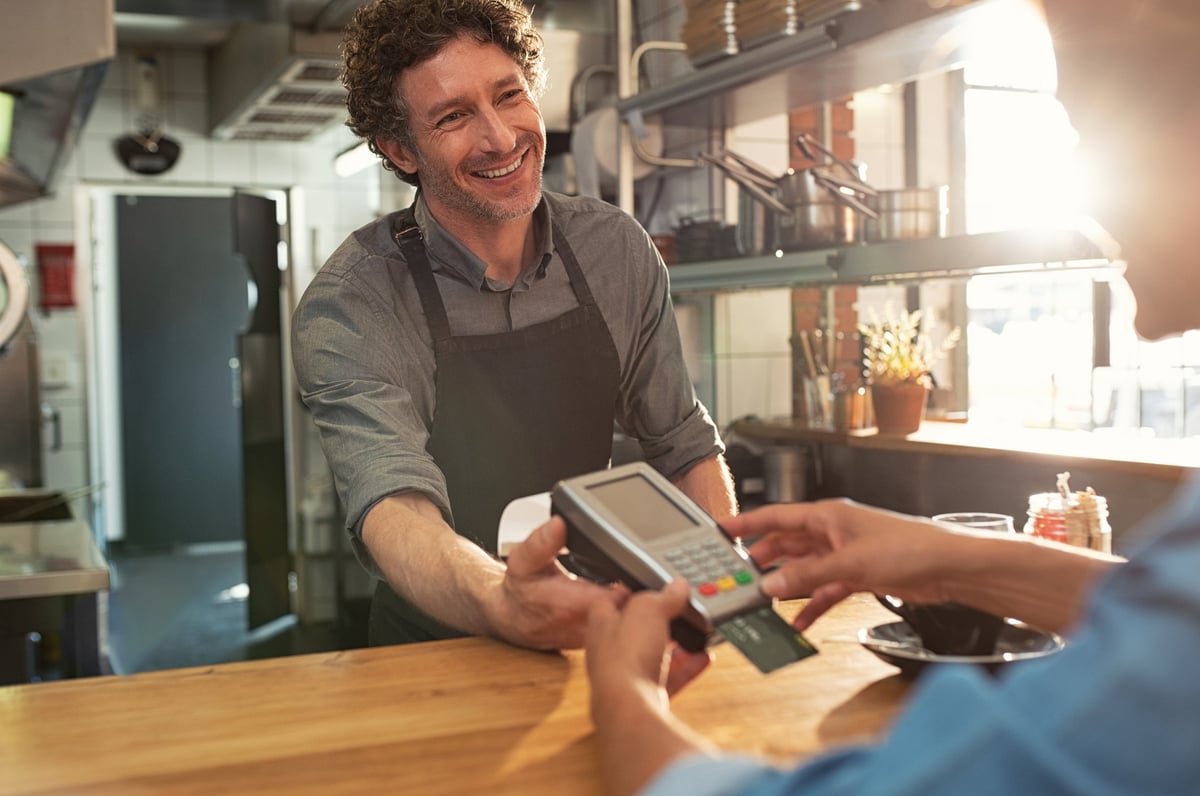 A cafe employee holding a credit card reader while the customer enters their PIN.
