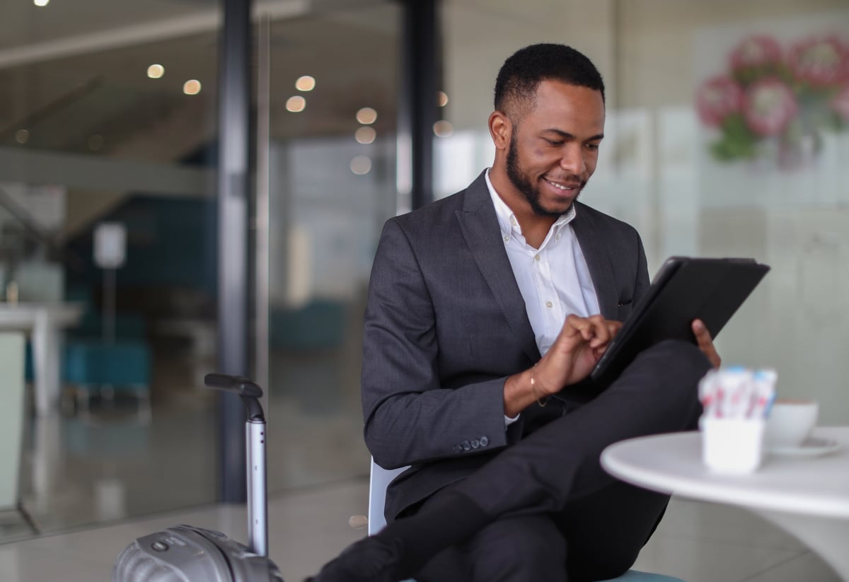 A man in a suit sits at a table and looks at his tablet.