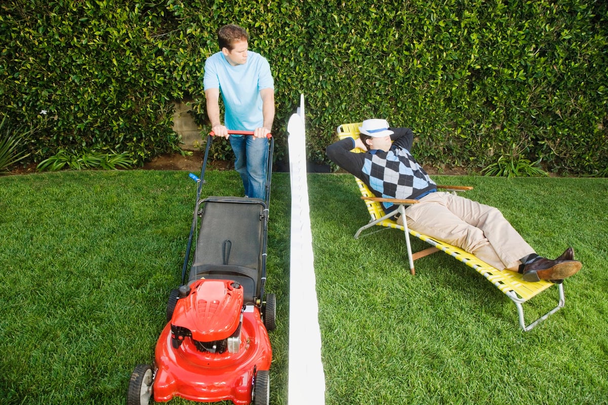One man mows his yard while his neighbor relaxes in his own yard.