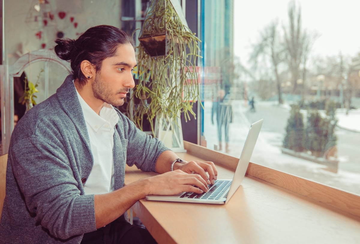 A man working on a laptop while sitting at a window table.