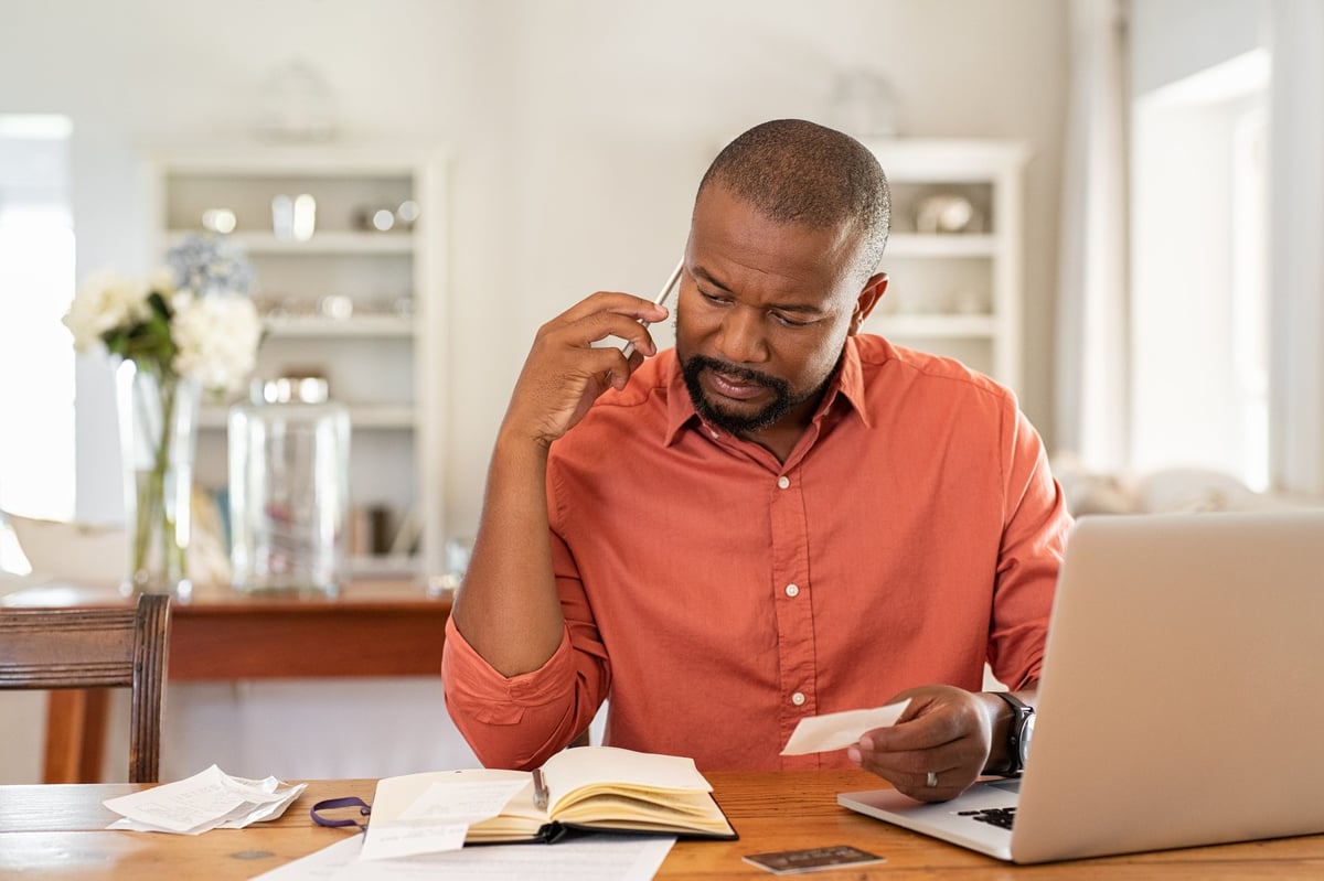 A man on the phone with a laptop and documents in front of him.