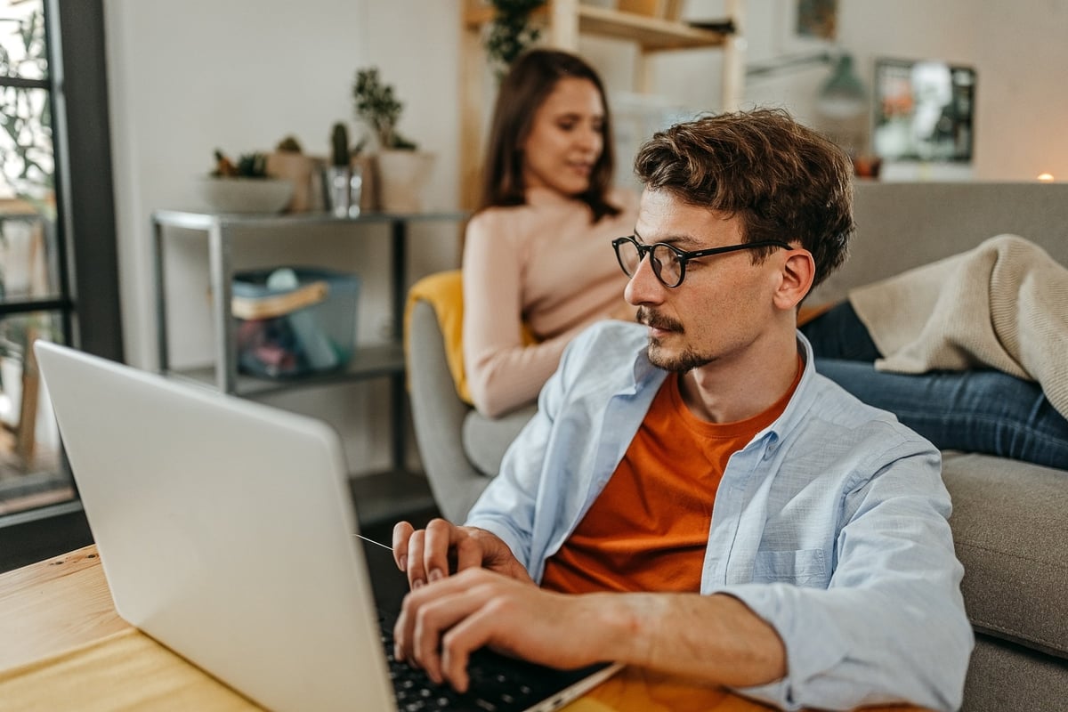 A man sits and reads the latest crypto news while his girlfriend reads in the background.