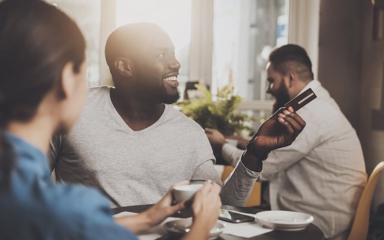 A man holding out a credit card with a smile at a restaurant.