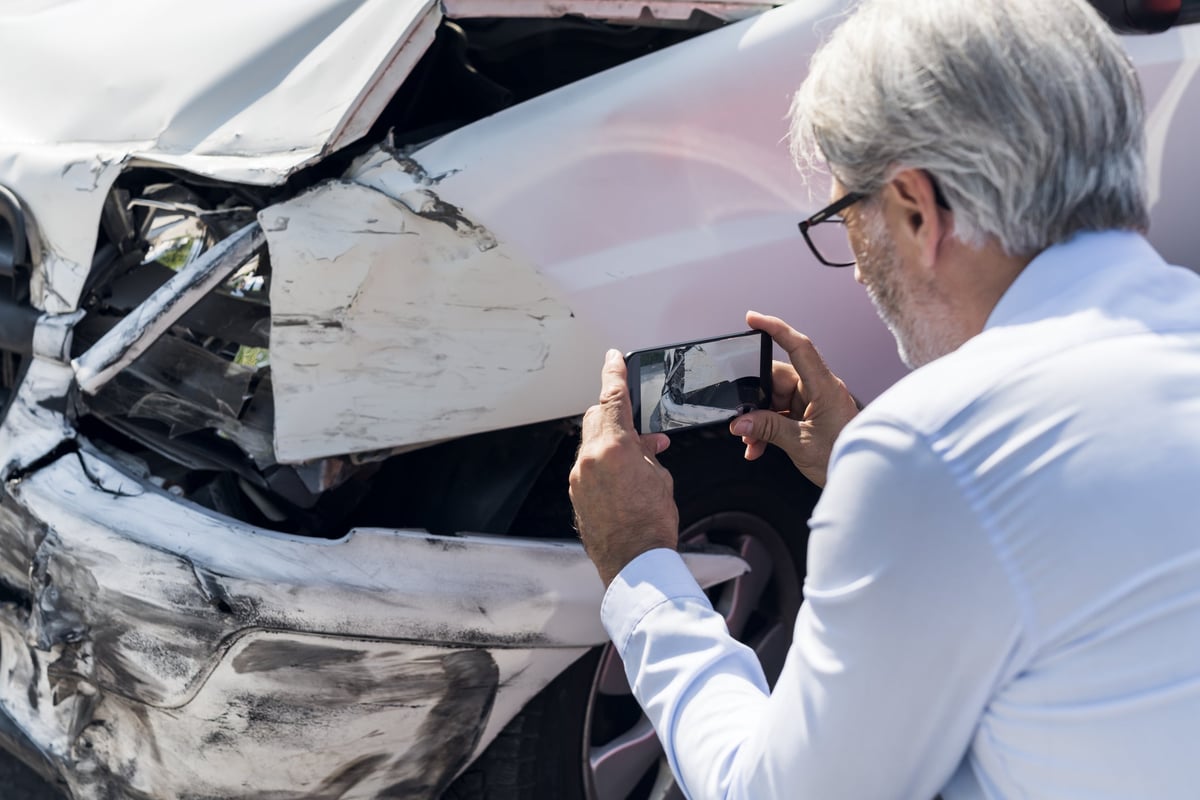 Man taking photos of damage to a vehicle.