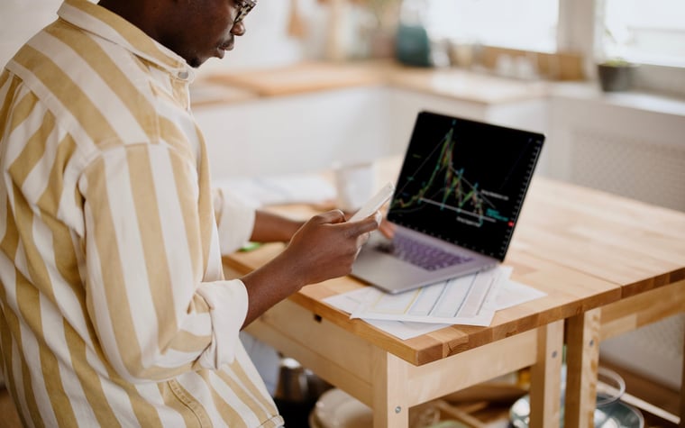 Man tracking downward performance on his laptop and also using his cell phone.