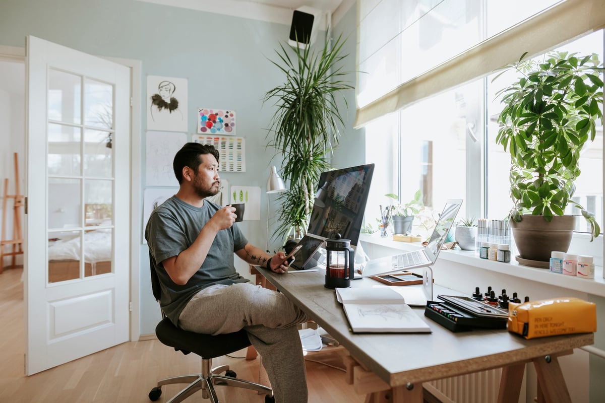 A man, working from home, sips his coffee and looks at his computer screen.