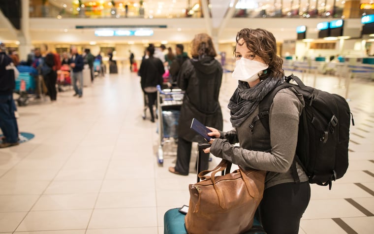 Masked woman with luggage waiting in a busy airport.