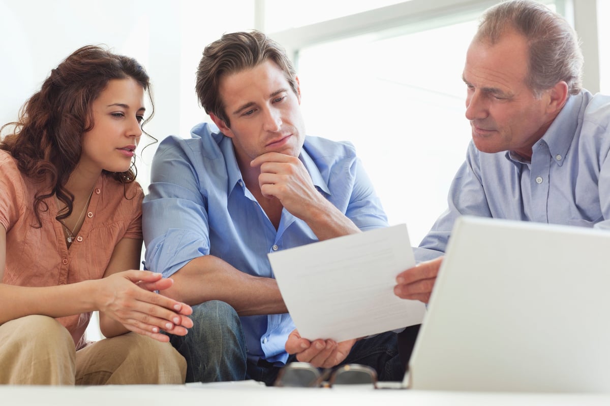 Mature man going over paperwork with young couple.