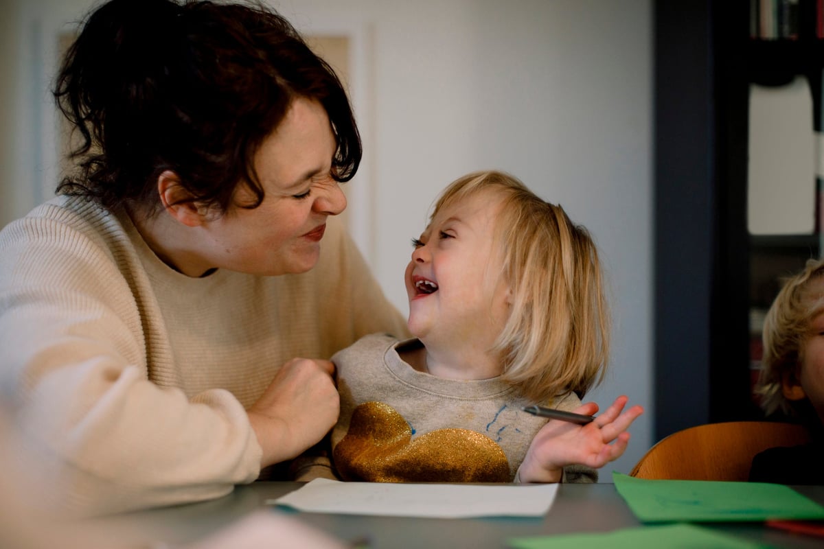 Mother making facial expressions while playing with disabled daughter at dining table.