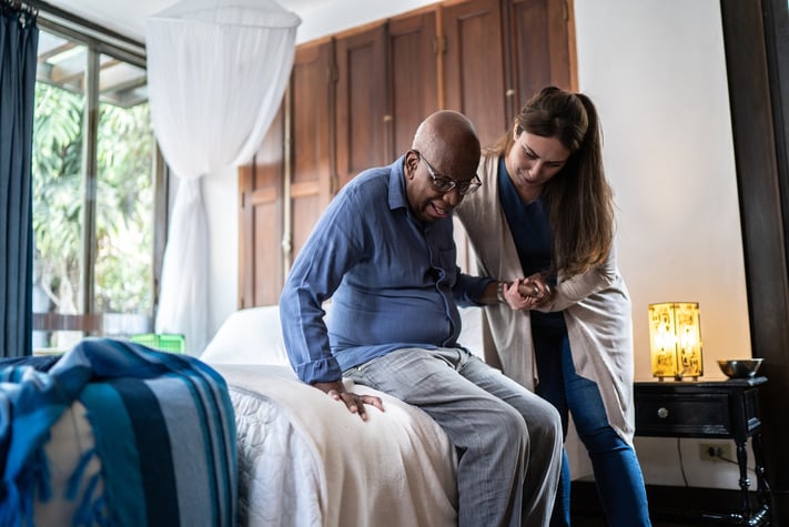 Nurse helping elderly man from bed in nursing home.