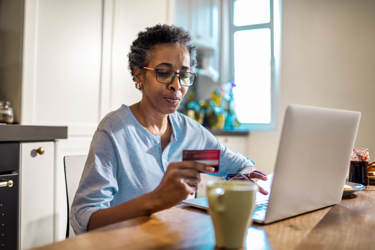 An older woman contemplates using her credit card to make an online purchase.