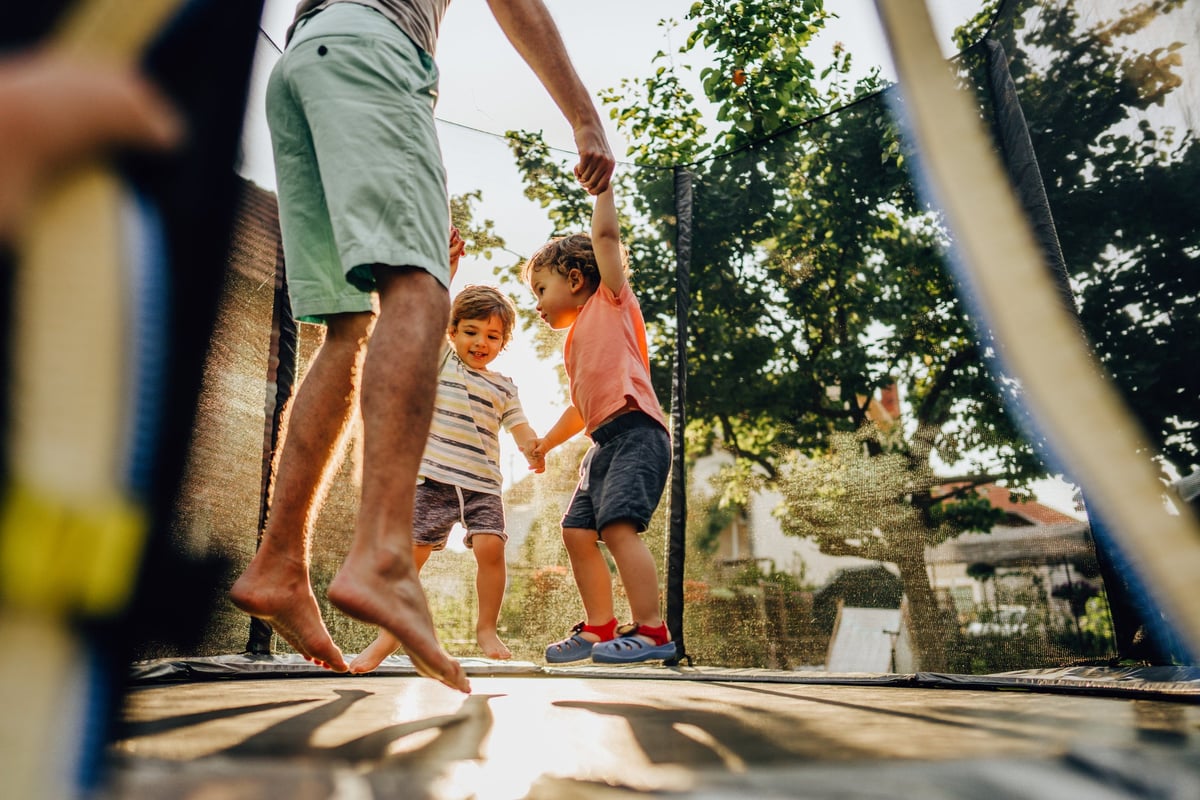 Parent jumping on trampoline with two small children.