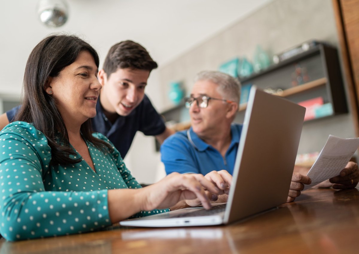 A child offers cryptocurrency advice to his parents who sit at a computer, looking over their personal finances.